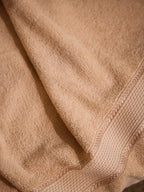 A close-up of a soft beige cotton towel with a textured waffle-weave border and folded drapery.